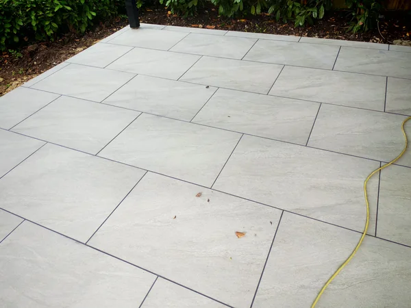 Large-format grey porcelain terrace laid to fall with an open-joint drainage channel